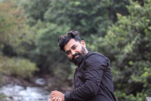 Portrait of an Indian man wearing a black shirt by a lush riverside in Nilambur, Kerala.