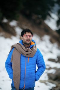 A man in a blue jacket with glasses stands outdoors in a snowy setting in Jammu and Kashmir.