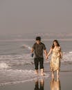 A couple walks hand in hand along a serene beach at sunset, capturing a moment of leisure and romance.